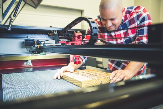 Operator loading an engraved wood sign into a Boss CO2 laser