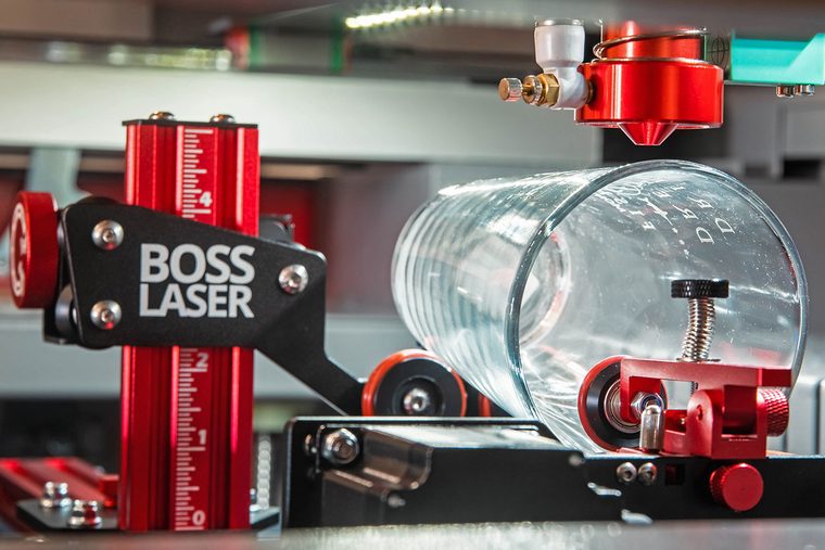 Glass tumbler mounted in a PiBurn rotary being engraved on a Boss laser